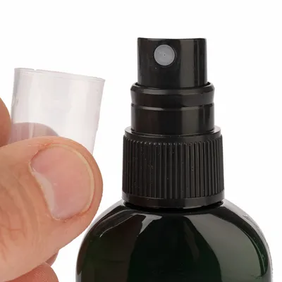 Flacon pulvérisateur noir avec bouchon transparent retiré, gros plan sur la pompe et le goulot. Aucun texte ou marque visible.