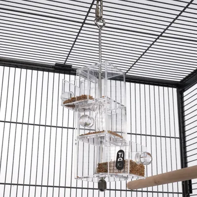 Distributeur transparent en plastique suspendu dans une cage à oiseaux, compartiments remplis de graines, marque TIAKI visible sur l’un des bacs.