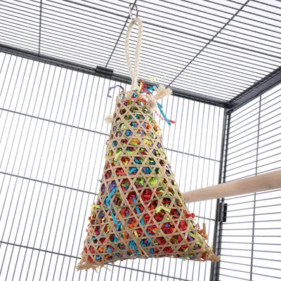 Jouet suspendu en forme de cône pour cage, structure en bois tressé avec lanières colorées à l’intérieur, corde épaisse pour accrocher. Perchoir en bois visible à côté.