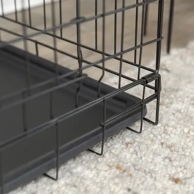 Detailaufnahme eines schwarzen Metallkäfigs mit herausnehmbarer Kunststoffwanne auf Teppichboden.