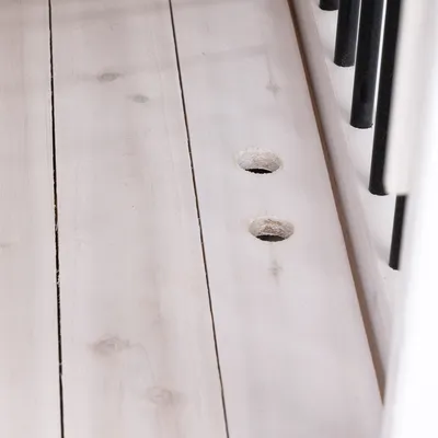 Nahaufnahme von zwei gebohrten Löchern in hellem Holz neben schwarzen Metallstäben, zeigt Details der Verarbeitung oder Montage.