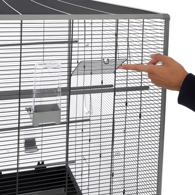 Hand pointing at a removable grid door of a birdcage with integrated transparent plastic feeder.