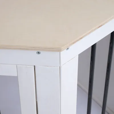 Ecke eines weissen Holztisches mit hellem Holzplatte und schwarzen Metallstreben. Schrauben sichtbar an der Verbindung.