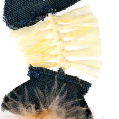 Gros plan sur un jouet pour animal en tissu noir, raphia jaune et fausse fourrure beige, montrant les matériaux utilisés.