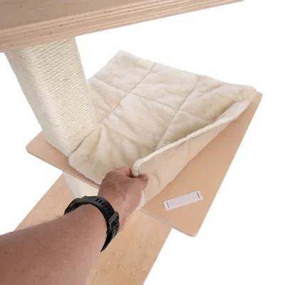 Mano muestra superficie de descanso acolchada y desmontable de tela suave sobre una plataforma de madera de un árbol rascador.