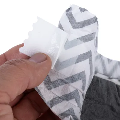 Nahaufnahme einer Hand, die den Klebestreifen eines grauen und weißen Produkts mit Zickzackmuster abzieht.