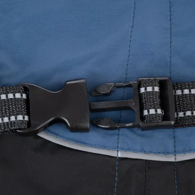 Close-up of an adjustable black plastic buckle and strap fastener attached to blue and black fabric, showing how the fastening mechanism works.
