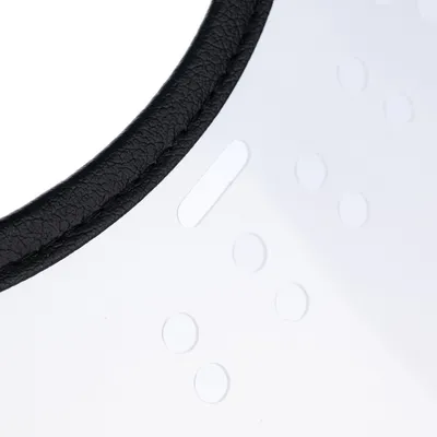 Gros plan sur un bord en similicuir noir cousu et une surface transparente avec des points en relief, matériaux visibles : similicuir et plastique.