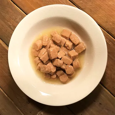 Valkoisella lautasella paloiteltua märkäruokaa hyytelössä tai kastikkeessa, ei näkyvää tuotemerkkiä tai pakkausta.