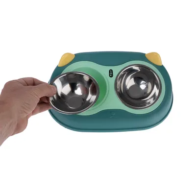 Double bowl made of stainless steel with green plastic holder, removable. Hand shows easy removal of one bowl.