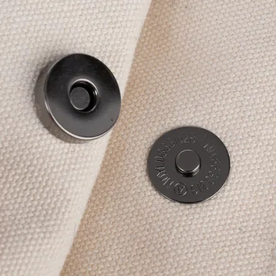 Vista detallada de dos cierres magnéticos sobre tela beige, adecuados para bolsos o accesorios.
