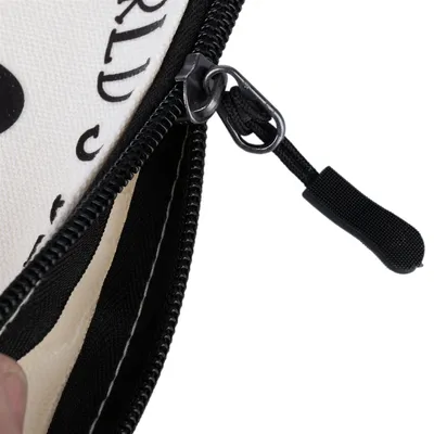 Gros plan sur une fermeture éclair noire en tissu sur une pochette blanche avec texte partiellement visible.