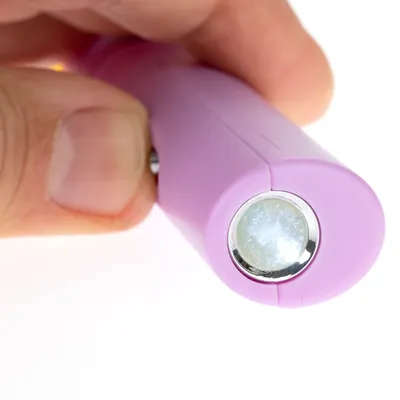 Nærbillede af en lyserød laserpointer med sølvfarvet knap, holdt af en hånd.