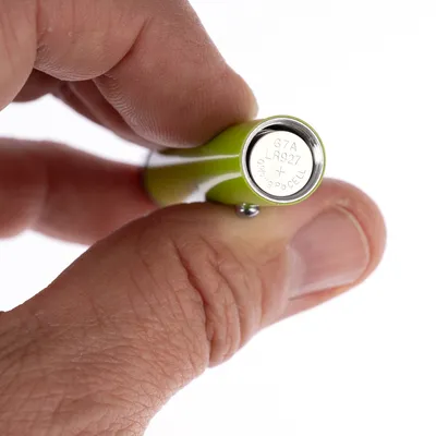 Nærbillede af et grønt batteri med teksten G7A LR927, 0% Hg Pb Cell, holdt mellem to fingre.