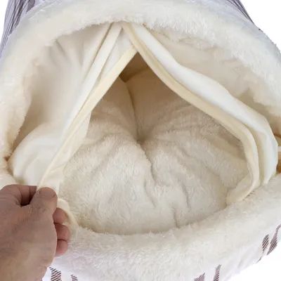 Intérieur d’un tunnel ou sac de couchage pour animal, tissu doux crème, main soulevant l’ouverture pour montrer le coussin moelleux à l’intérieur. Matière visible : tissu peluche.