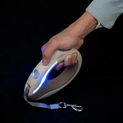 Mano che tiene un guinzaglio beige per cani con luce LED e moschettone in metallo, adatto per passeggiate al buio.