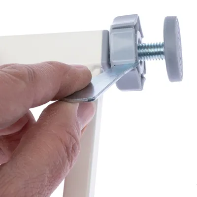 Main serrant une clé plate sur une vis de réglage en métal et plastique gris, fixée à un cadre blanc. Outil visible pour montage ou ajustement.