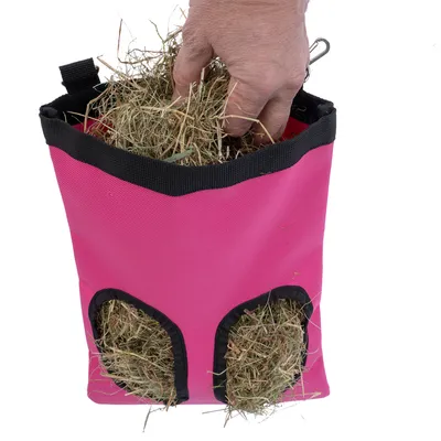 Bolsa de heno rosa con dos aberturas, llena de heno. Una mano mete la mano en la bolsa.