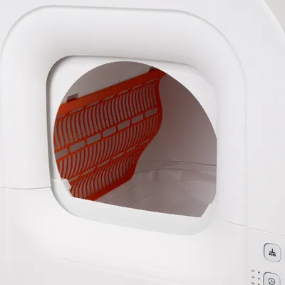Interior view of a white cat toilet with orange sieve insert and control elements on the side.