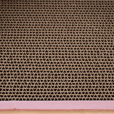Surface en carton ondulé vue de près, structure alvéolée marron avec bordure rose visible en bas de l’image.
