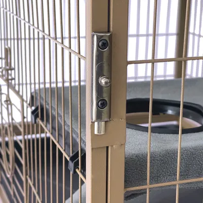 Detaljan prikaz metalne kopče na bež kavezu sa sivom površinom za ležanje i integriranom zdjelicom za hranu.