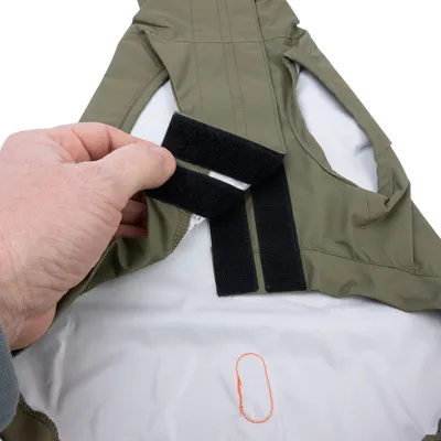 Nahaufnahme eines olivgrünen Stoffstücks mit Klettverschluss, das von einer Hand geöffnet wird. Weisser Innenstoff und orangefarbene Naht sichtbar.