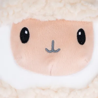 Close-up van een pluchen speelgoed met schapengezicht, geborduurde zwarte ogen en grijze mond op beige stof.