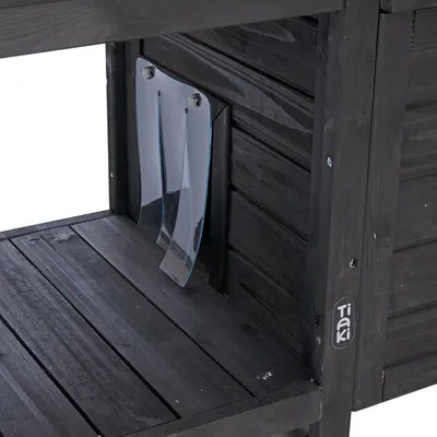 Schwarzes Holzhaus mit transparenter Kunststoffklappe, Tiaki-Logo sichtbar auf der Seite.