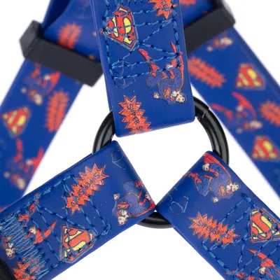 Niebieskie szelki dla psa z motywami Superman i czerwonymi elementami komiksowymi, połączone czarnym metalowym kółkiem.
