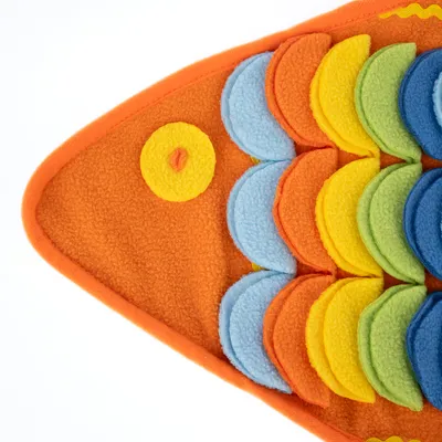 Zabawka w kształcie ryby z pomarańczowej tkaniny z kolorowymi filcowymi łuskami w niebieskim, żółtym, zielonym i pomarańczowym kolorze. Odpowiednia do interaktywnej zabawy.