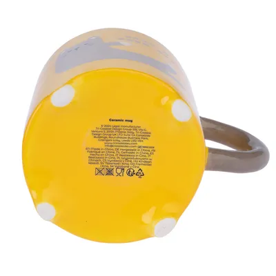 Fond d’une tasse en céramique jaune avec texte multilingue, pictogrammes d’entretien et mention « Ceramic mug ». Poignée marron visible sur le côté droit.