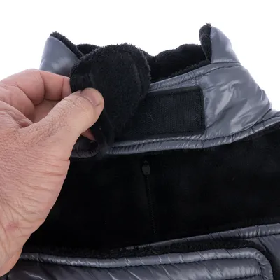Gros plan sur une main ouvrant la fermeture velcro d’un manteau pour chien en tissu matelassé gris et doublure noire en polaire, avec une fermeture éclair visible.