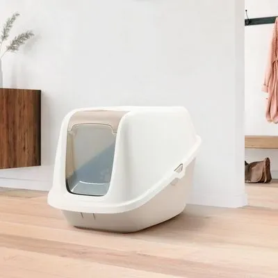 Gesloten kattenbak van wit plastic met transparant klapdeurtje, geplaatst op een houten vloer in een moderne ruimte. Geen merknaam of extra tekst zichtbaar.