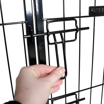 Hand zeigt, wie der Verschluss eines schwarzen Metallgitters geöffnet wird.