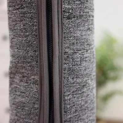 Gros plan sur une fermeture éclair noire sur tissu gris texturé, montrant le détail du matériau et de la couture.