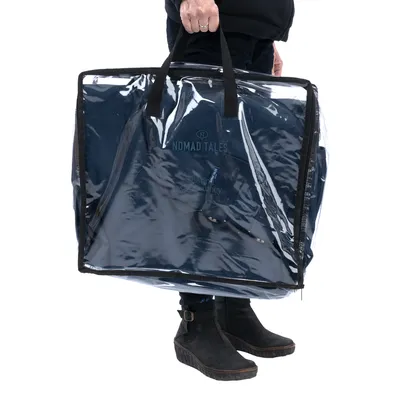 Nomad Tales Tragetasche mit transparentem Schutz, dunkelblau. Person hält die Tasche am Griff.
