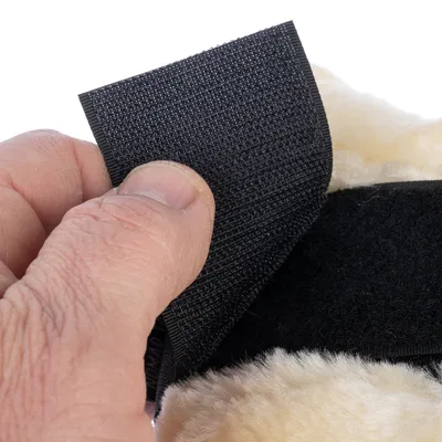 Gros plan sur une main ouvrant une fermeture à scratch noire fixée sur un tissu beige duveteux, montrant le système d’attache en plastique et textile.