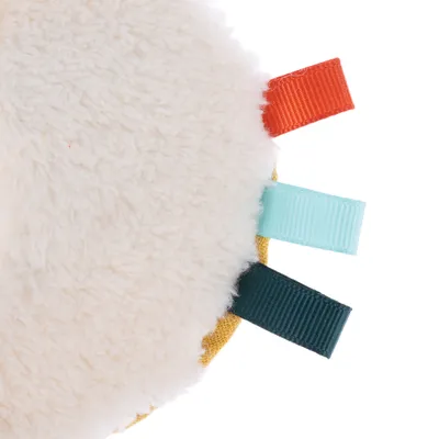 Round plush toy with soft surface and coloured fabric tabs in red, light blue and dark green.
