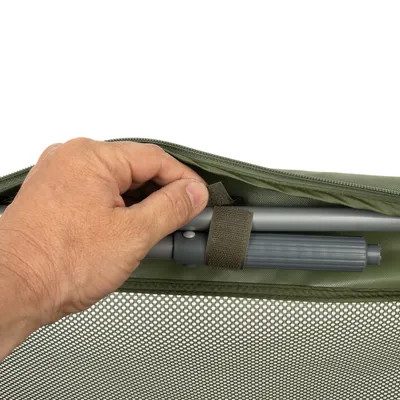 Mano muestra la fijación de una barra metálica gris con cierre de velcro en un bolso verde con material de malla.
