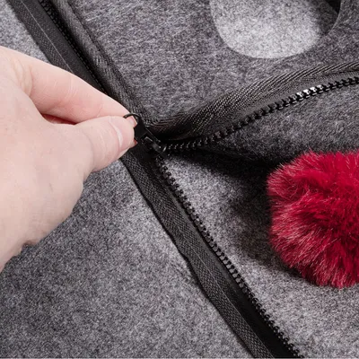 Hand opening a black zip on grey felt material with red plush ball. Close-up of a product with zip function.