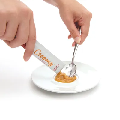 Käsi puristaa kermaista välipalaa 'Creamy'-tekstillä varustetusta tikusta lautaselle ja levittää sitä lusikalla. Käsi puristaa kermaista välipalaa 'Creamy'-tekstillä varustetusta tikusta lautaselle ja levittää sitä lusikalla.
