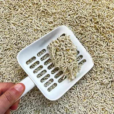 Clumping litter being scooped with a white slotted scoop, showing how the product forms solid clumps for easy cleaning.