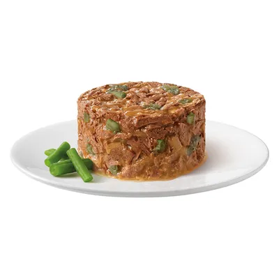 Annospala ruskeaa hyytelömäistä lemmikkiruokaa, jossa vihreitä paloja, tarjoiltuna valkoisella lautasella. Vieressä muutama vihreä papu.