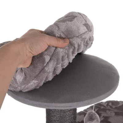 Main tenant un coussin gris amovible en tissu doux sur une plateforme ronde d’arbre à chat, poteau recouvert de corde visible en dessous.
