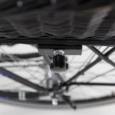 Gros plan sur le système de fixation en métal et plastique noir sous un panier fixé à la structure d’un vélo, avec roue visible en arrière-plan.