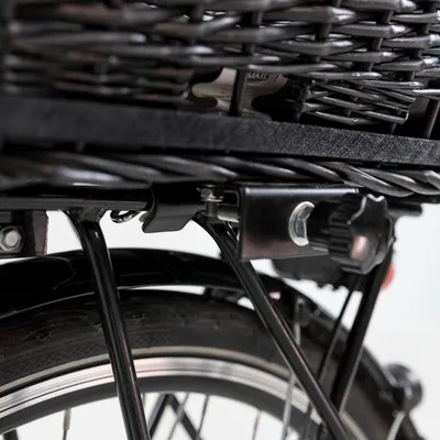Fixation en métal d’un panier en osier sur un porte-bagages de vélo, vue rapprochée montrant la molette de serrage et les tiges métalliques du support.