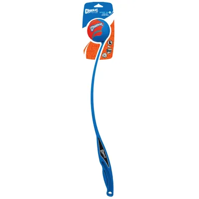 Chuckit! Sport 26 L -pallonheittäjä ja oranssi Chuckit!-pallo, koko L, pakkauksessa. Kahvassa musta yksityiskohta, pakkauksessa näkyy tuotemerkki ja kokomerkintä.