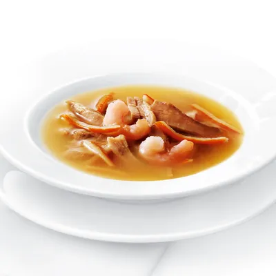 Primer plano de un bol con trozos de carne y gambas en caldo, servido en un plato blanco.