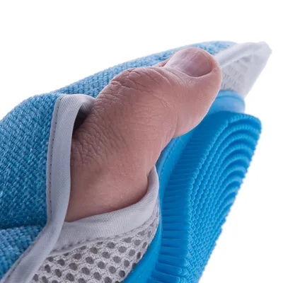 Nahaufnahme einer Hand, die eine blaue Bürste mit weichem Stoffgriff und flexiblen Borsten hält.