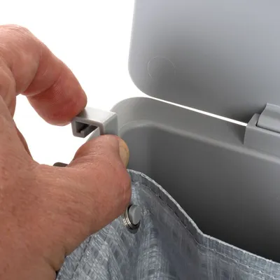 Hand bevestigt grijze kunststof clip aan rand van een open grijze bak met inzetzak van geweven kunststof. Detail van bevestigingssysteem zichtbaar.